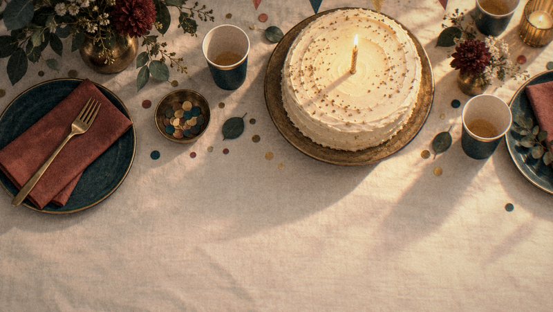 A party table seen from above with bunting, a candlelit cake and confetti.