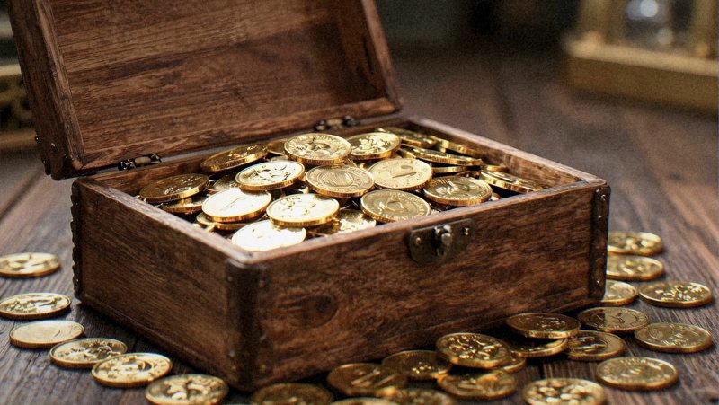 An open wooden chest with brass banding, gold coins spilling out.